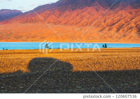 Road trip through national natural parks of central asia. Shadow of a car on arid steppe land against the backdrop of lake bartogay near tian shan mountains. Road trip through national natural parks of central asia. Shadow of a car on arid steppe land against the backdrop of lake bartogay near tian shan mountains. 120607536