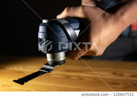 A person holds a versatile oscillating Multi Cutter tool, ready to tackle detailed woodworking or renovation tasks 120607552