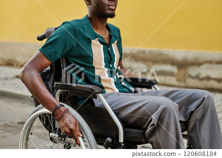 Vibrant cropped shot of smiling African American man using wheelchair outdoors moving against yellow wall in city copy space 120608184