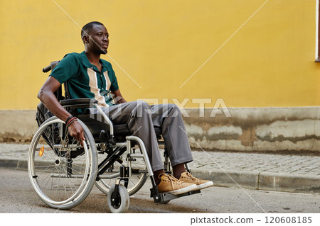 Vibrant full length portrait of African American man with disability using wheelchair outdoors moving against yellow wall in city copy space Vibrant full length portrait of African American man with disability using wheelchair outdoors moving against yellow wall in city copy space 120608185