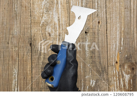 A hand firmly grasping a unique and finely crafted blade tool set against a rustic wooden backdrop 120608795