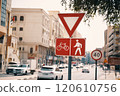 A bustling city street with a bicycle and pedestrian sign, surrounded by buildings and trees. Vehicles and pedestrians share the road in this urban setting 120610756