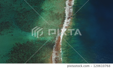 Breathtaking aerial view of green and turquoise water waves gently breaking coral reef barrier, creating stunning contrast between shallow and deep blue ocean. Wild nature beauty. Natural background 120610768