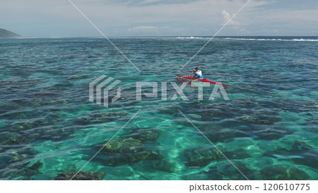 Aerial drone captures a sportsman kayaking in the crystal-clear turquoise waters of Tahiti. French Polynesia. Showcasing the vibrant coral reef below and the lush green island in the distance Aerial drone captures a sportsman kayaking in the crystal-clear turquoise waters of Tahiti. French Polynesia. Showcasing the vibrant coral reef below and the lush green island in the distance 120610775