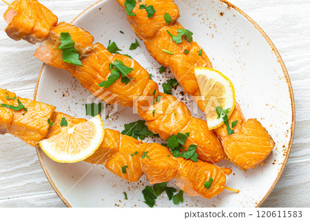 Grilled barbecue salmon skewers seasoned with green parsley and lemon on ceramic plate on white wooden rustic table background top view, healthy eating 120611583
