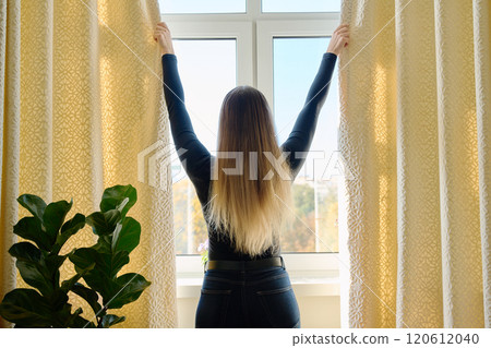 Young woman closing opening thick curtains on window Young woman closing opening thick curtains on window 120612040