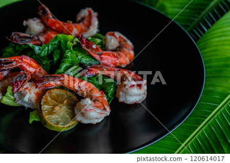 Succulent grilled tiger shrimp are elegantly arranged atop vibrant banana leaves, accompanied by fresh greens and a slice of lime, creating a feast for the senses. 120614017