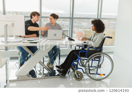 Teamwork brainstorm. Diverse multiracial colleagues woman in chair for people with disability working together. Group of people sitting in creative office discussing business. Young professional team 120614193