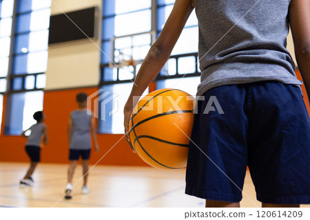 Holding basketball, boy watching classmates playing game in school gymnasium, copy space Holding basketball, boy watching classmates playing game in school gymnasium, copy space 120614209