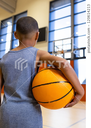 In school gym, boy holding basketball, looking at hoop, preparing to play 120614213