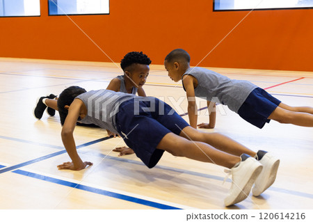 In school gym, three multiracial boys doing push-ups together during physical education class 120614216