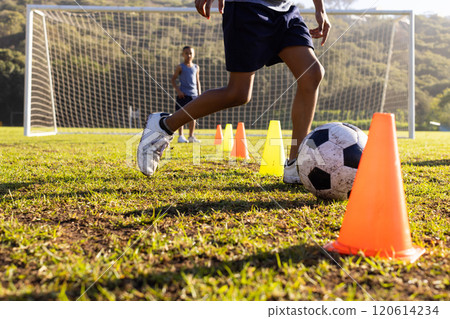 Outdoors, dribbling soccer ball through cones, multiracial boys practicing football at school field 120614234