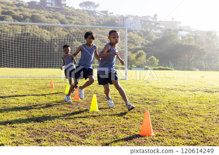 Outdoors, running through cones, multiracial boys training on school soccer field 120614249