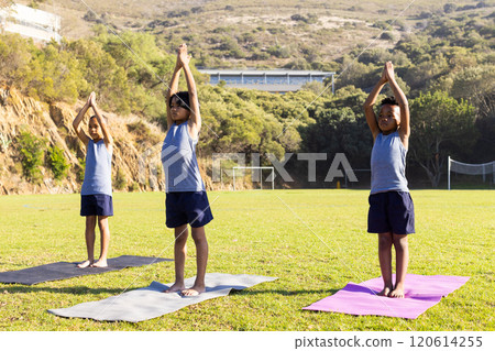 Practicing yoga, three multiracial boys standing on mats outdoors at school field Practicing yoga, three multiracial boys standing on mats outdoors at school field 120614255