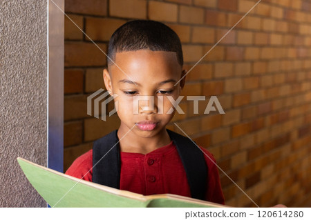 In school, boy reading notebook while standing against brick wall In school, boy reading notebook while standing against brick wall 120614280