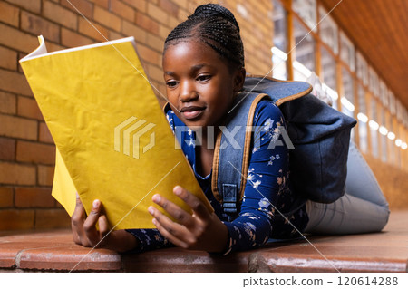 In school, african american girl lying on floor reading yellow notebook with backpack on In school, african american girl lying on floor reading yellow notebook with backpack on 120614288