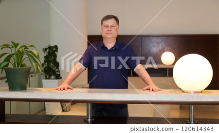 Front desk worker, adult male 45-50 years old in short sleeve shirt, standing at work station 120614343