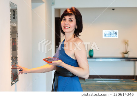 A woman in a blue dress calls the elevator to her floor of the house 120614346