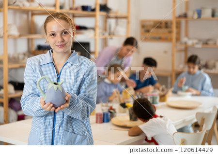 Girl holds a clay product against the background of students and a teacher Girl holds a clay product against the background of students and a teacher 120614429