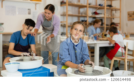 Children working at potter's wheel with teacher in art studio 120614498