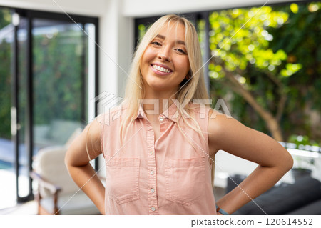 Smiling woman in casual attire standing confidently in bright living room 120614552