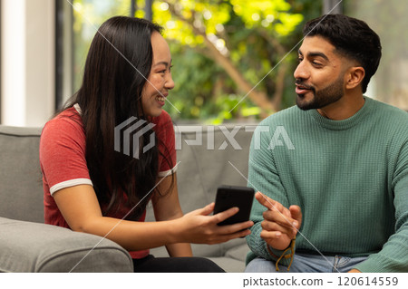 Diverse friends sitting on couch, talking and using smartphone, enjoying conversation Diverse friends sitting on couch, talking and using smartphone, enjoying conversation 120614559