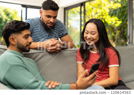 Diverse friends sitting on couch, looking at smartphone, smiling and enjoying time together Diverse friends sitting on couch, looking at smartphone, smiling and enjoying time together 120614563