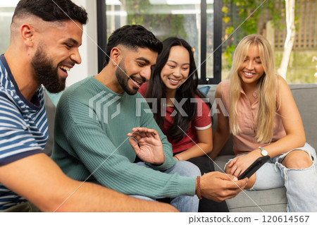 diverse friends sitting on couch, smiling and looking at smartphone together 120614567