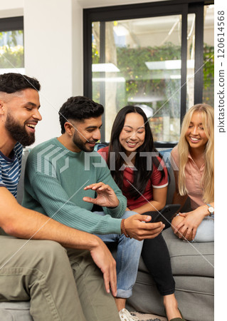 diverse friends sitting on couch, smiling and looking at smartphone together 120614568