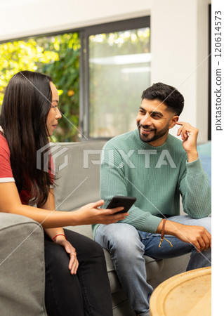 diverse friends sitting on couch, talking and using smartphone, enjoying conversation diverse friends sitting on couch, talking and using smartphone, enjoying conversation 120614573