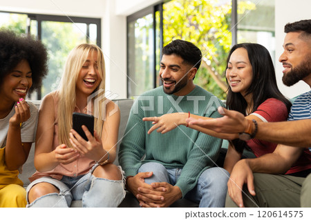 diverse friends sitting on couch, laughing and looking at smartphone together indoors diverse friends sitting on couch, laughing and looking at smartphone together indoors 120614575