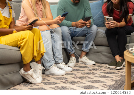 Sitting on couch, group of friends using smartphones, focusing on screens Sitting on couch, group of friends using smartphones, focusing on screens 120614583