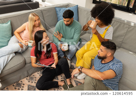 Group of young friends sitting on couch, drinking coffee, and talking together 120614595