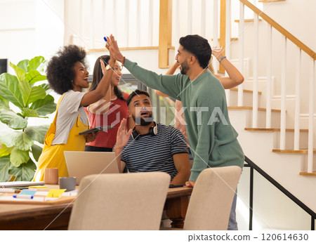 High-fiving, group of young friends celebrating success at home office desk 120614630