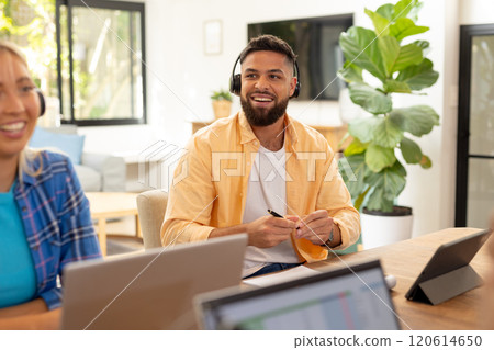 Smiling man wearing headphones working on laptop in modern office setting 120614650