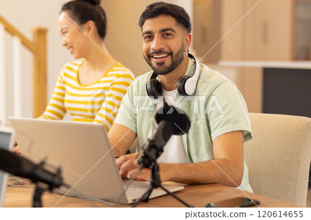 Smiling man using laptop with headphones and microphone, working from home 120614655
