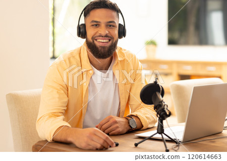 Smiling man recording podcast with microphone and laptop at home office 120614663