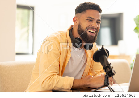 Smiling man with headphones recording podcast using microphone and laptop 120614665