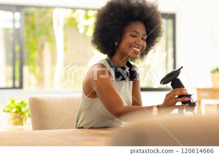 Adjusting microphone, smiling african american woman with headphones around neck preparing for podca 120614666
