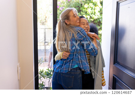Friends hugging and smiling, greeting each other warmly at front door 120614687