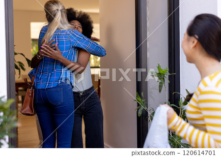 Friends hugging at doorway while another friend arrives, enjoying reunion 120614701
