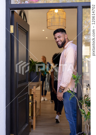 Welcoming friends, man smiling and standing at open door of house 120614702