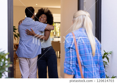 Hugging friend at doorway, woman smiling while another friend watches 120614703