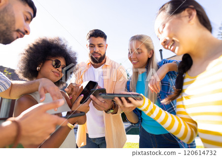 Group of young diverse friends using smartphones and tablets, enjoying outdoor time together 120614732