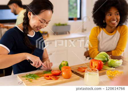 Chopping vegetables, woman smiling while preparing meal with diverse friends in kitchen 120614766