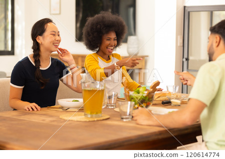 Friends laughing and pointing while enjoying meal together at dining table 120614774