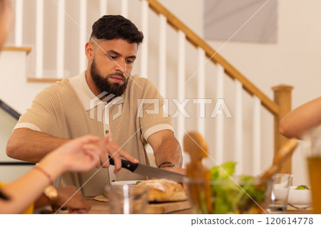 Cutting bread, man preparing meal with diverse friends at home dining table Cutting bread, man preparing meal with diverse friends at home dining table 120614778