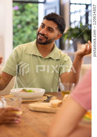 Smiling man enjoying meal with diverse friends, sitting at dining table, socializing 120614807
