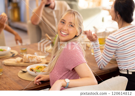 Smiling young woman sitting at dining table with diverse friends, enjoying meal together Smiling young woman sitting at dining table with diverse friends, enjoying meal together 120614812
