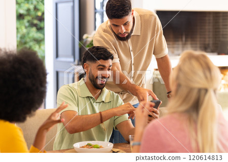 Friends gathered around table, smiling and looking at smartphone together Friends gathered around table, smiling and looking at smartphone together 120614813